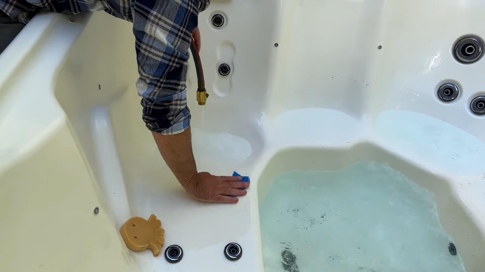 A man wiping down a hot tub with a cloth after draining the water