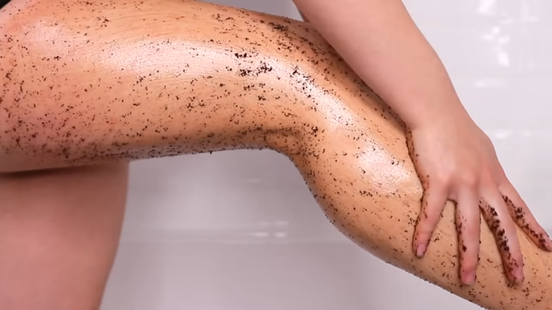 A Person Exfoliating Their Legs with A Coffee Scrub in A Bathroom