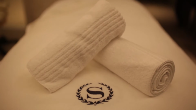 Two Neatly Rolled White Towels on A Spa Bed with An Embroidered "S" Logo