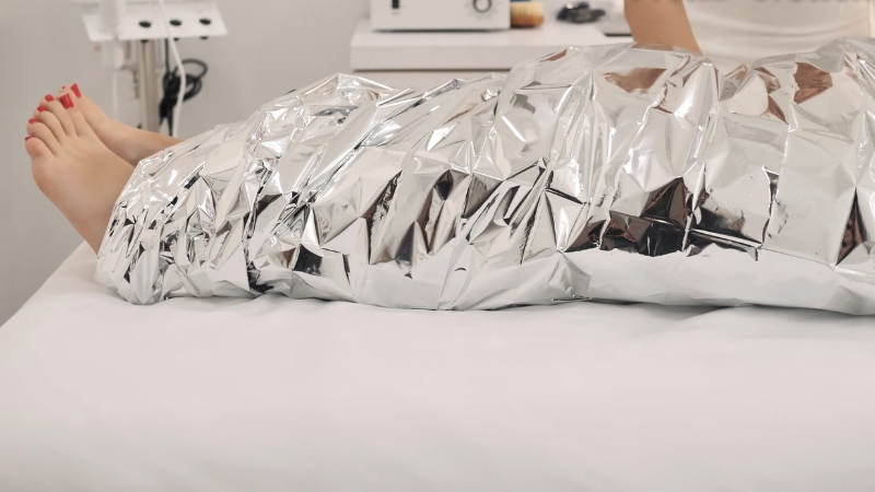 A Person’s Legs Wrapped in A Silver Thermal Blanket During a Spa Body Treatment