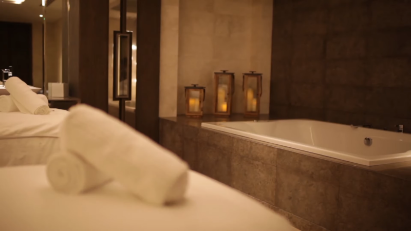 A Cozy Spa Room with Rolled White Towels, a Large Bathtub, and Soft Candlelight in Lanterns